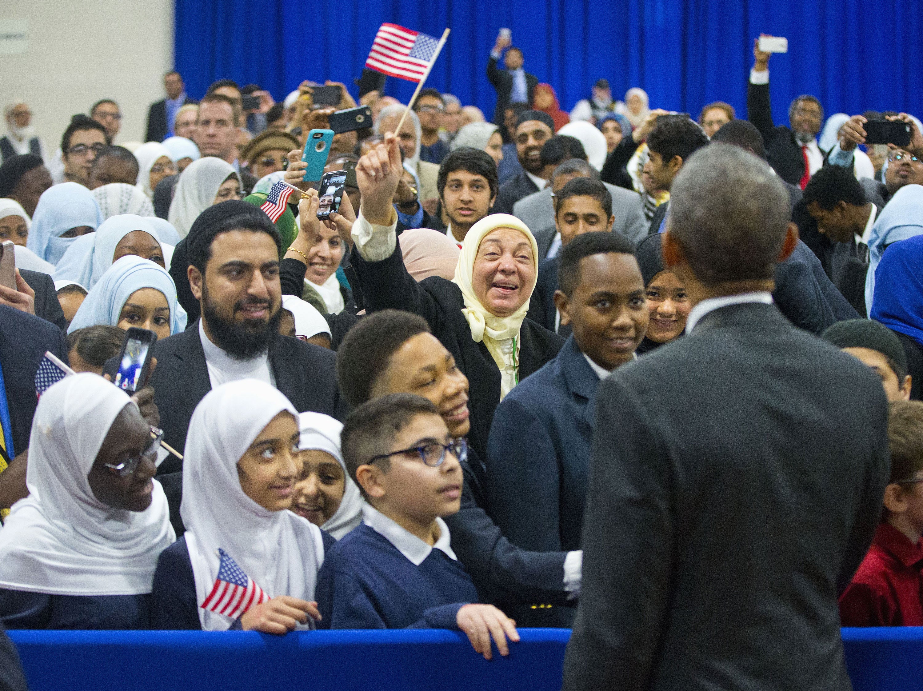 President Obama stands in front of a crowd of people, many of whom appear to be smiling and waving at him.