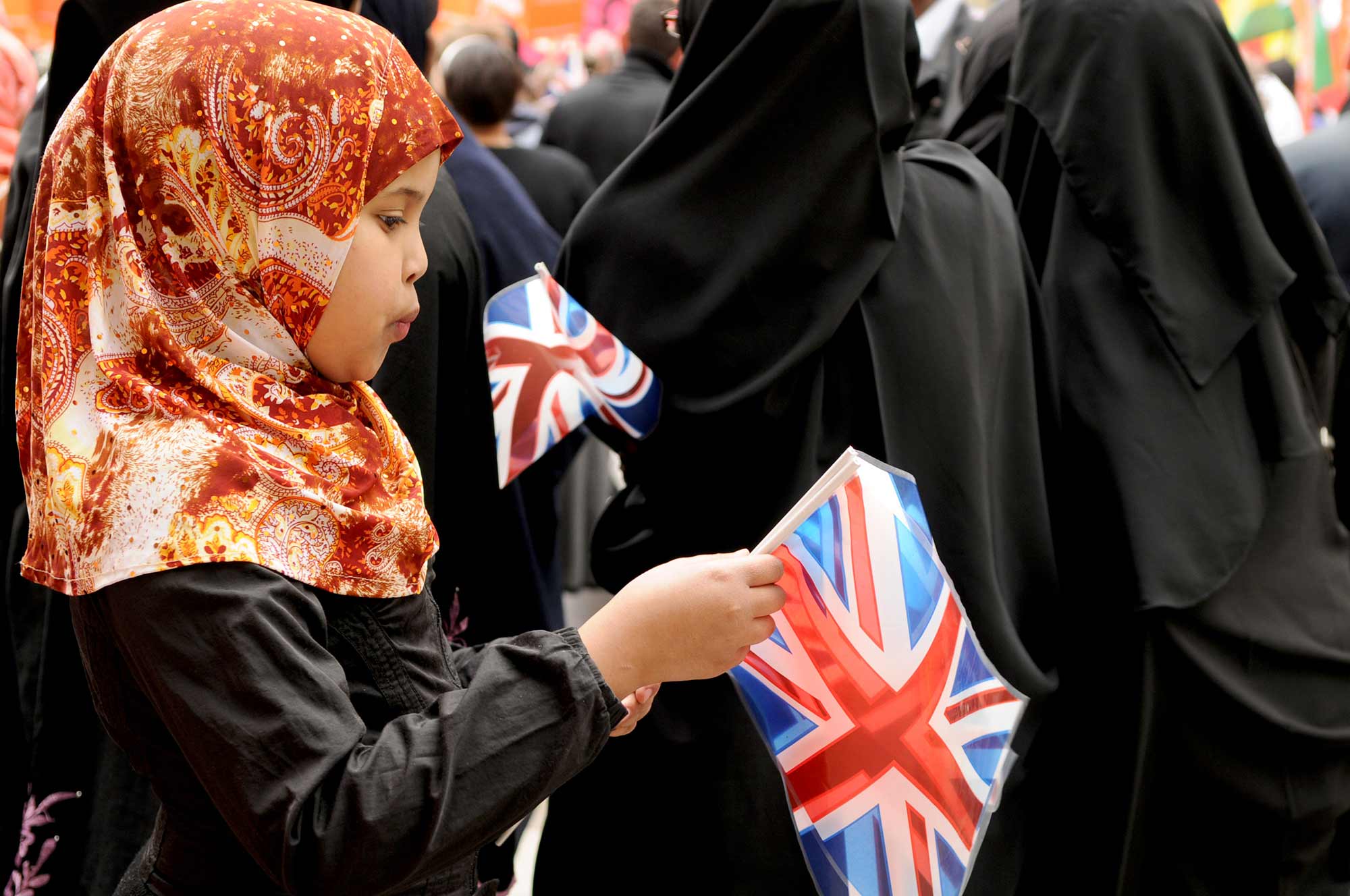 A young girl wearing a hijab holds a British flag in her hands.