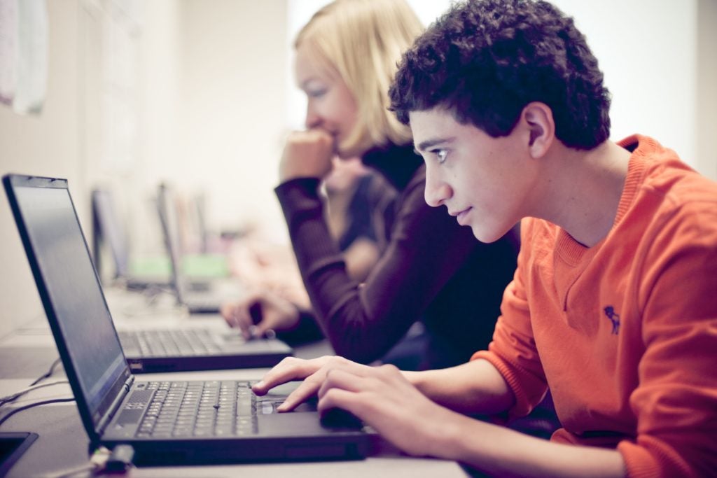 A young boy wearing an orange sweatshirt types on a laptop computer.