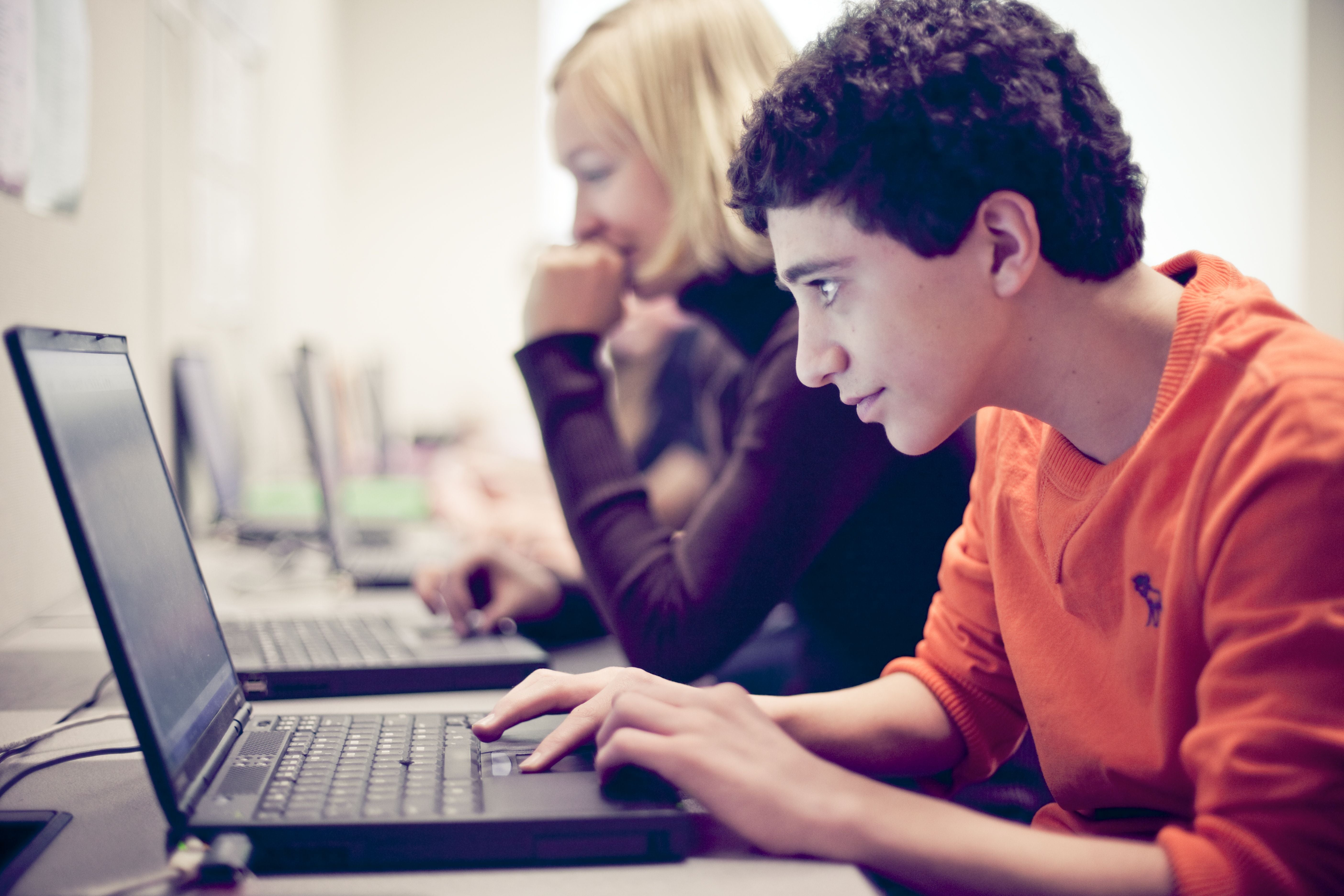 A young boy wearing an orange sweatshirt types on a laptop computer.