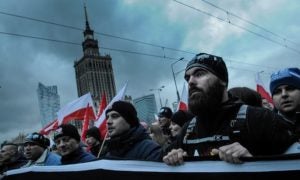 Protesters demonstrate in Poland and appear to hold up a large banner against a backdrop of a grey, cloudy sky.