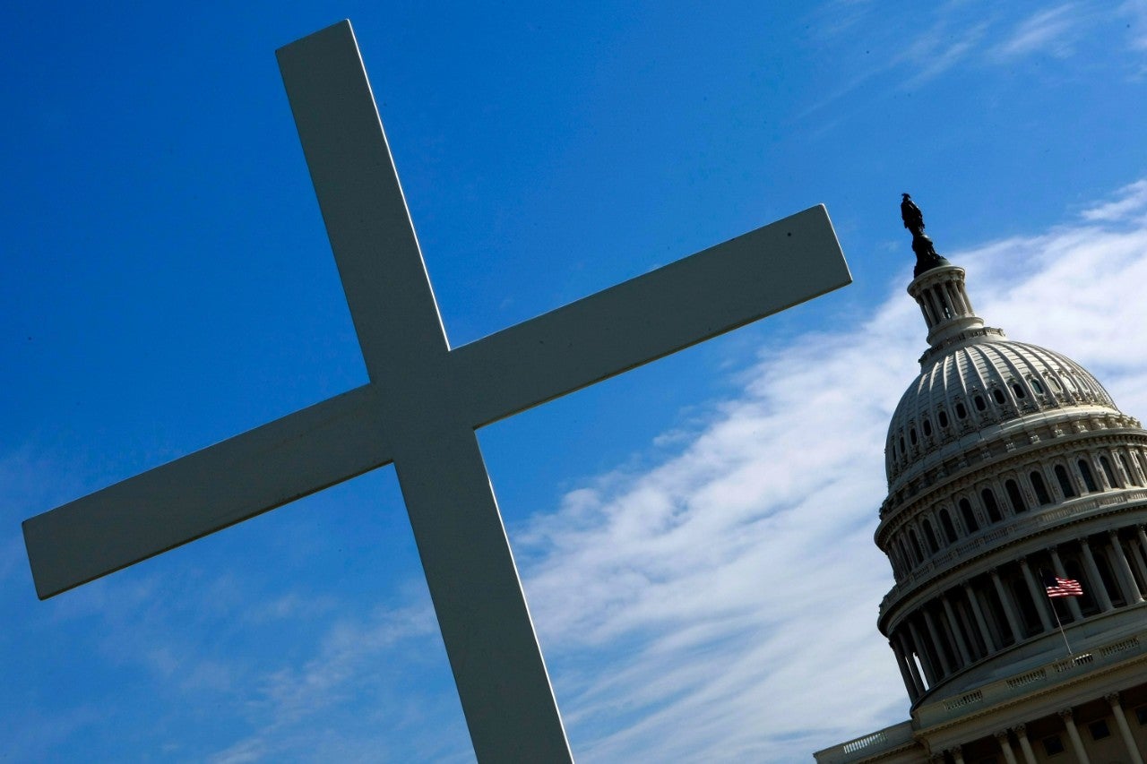 A cross appears in the foreground of an image of the U.S. Capitol Building.