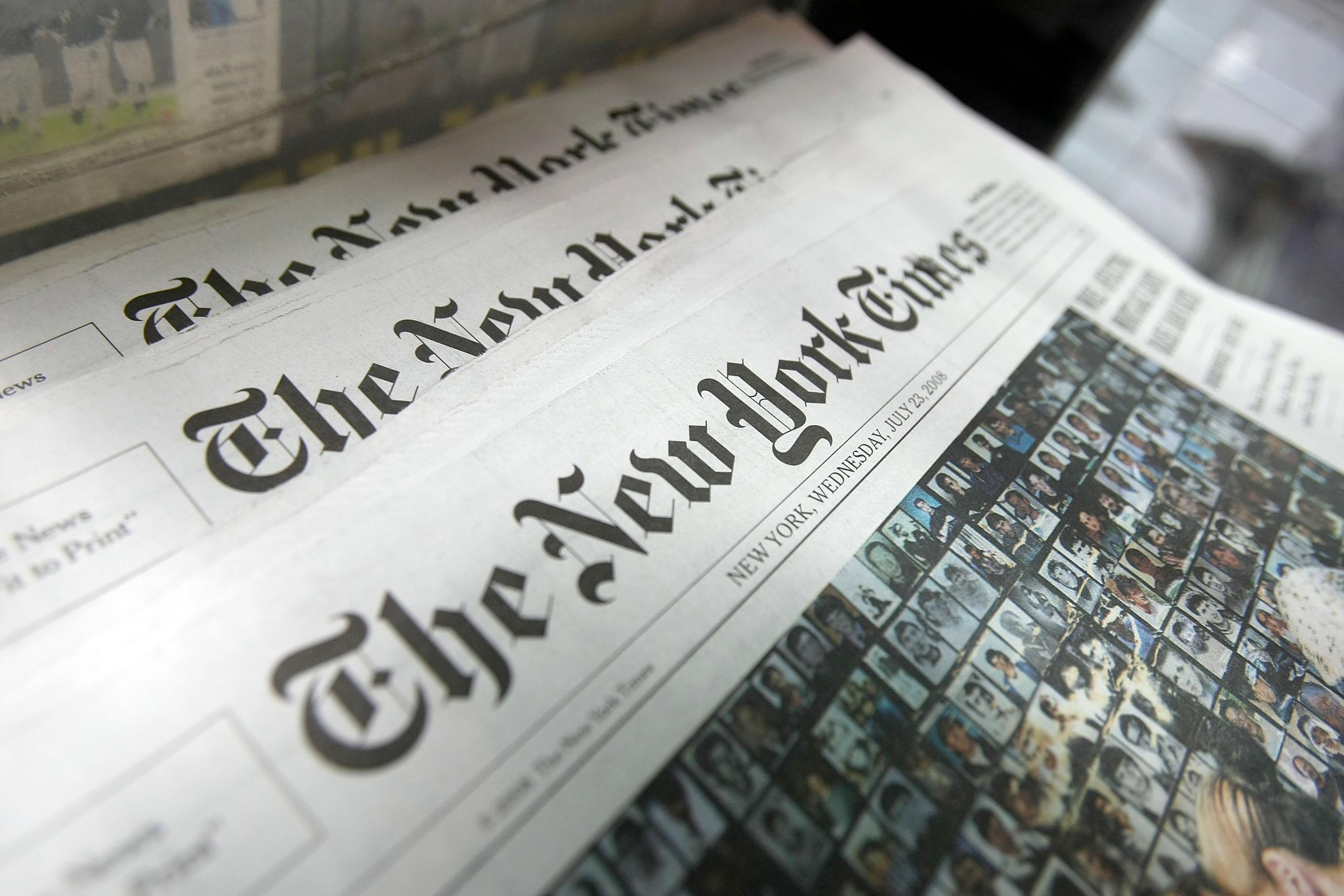 A stack of New York Times newspapers on a newspaper stand.