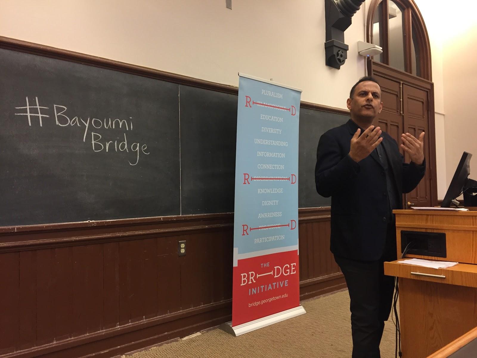 Professor Moustafa Bayoumi speaks at Georgetown University on April 25, 2017. The words "#BayoumiBridge" are written on a chalkboard in the background.
