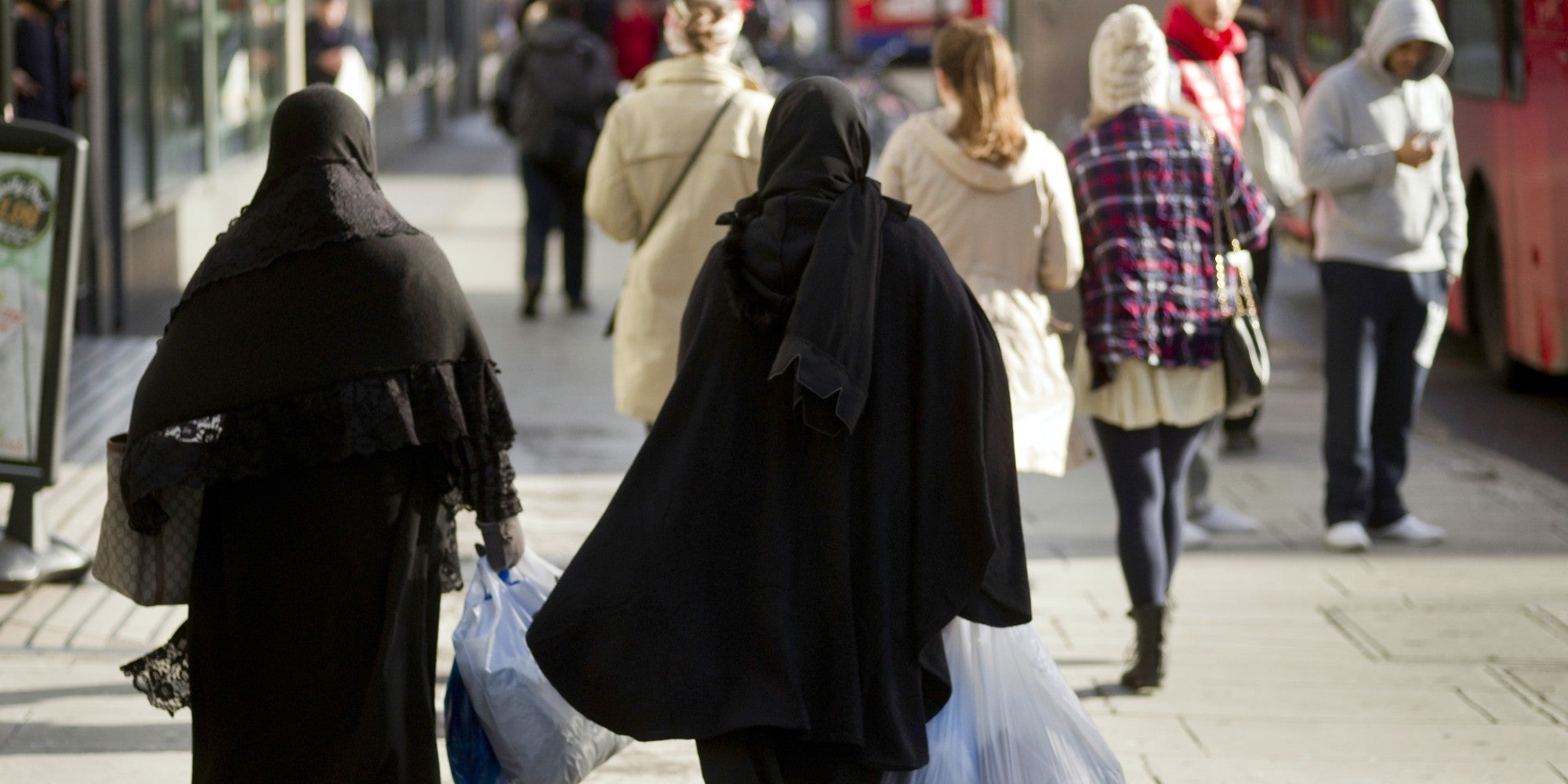 Two people wearing burqas walk with their backs facing the camera.