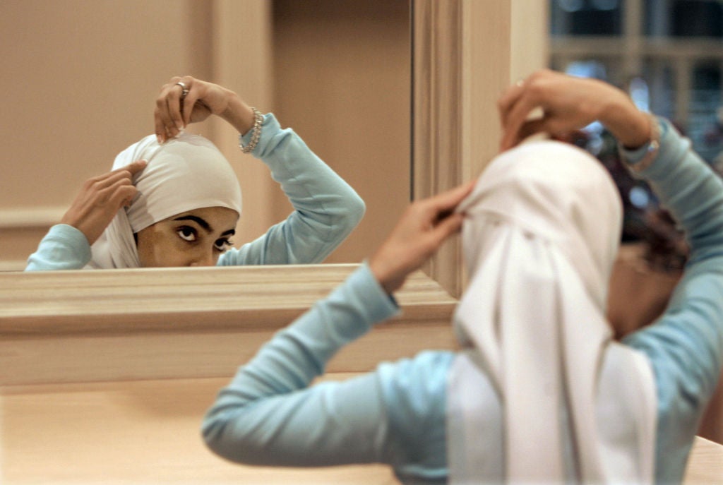 A person looks into the mirror while adjusting the hijab they wear.