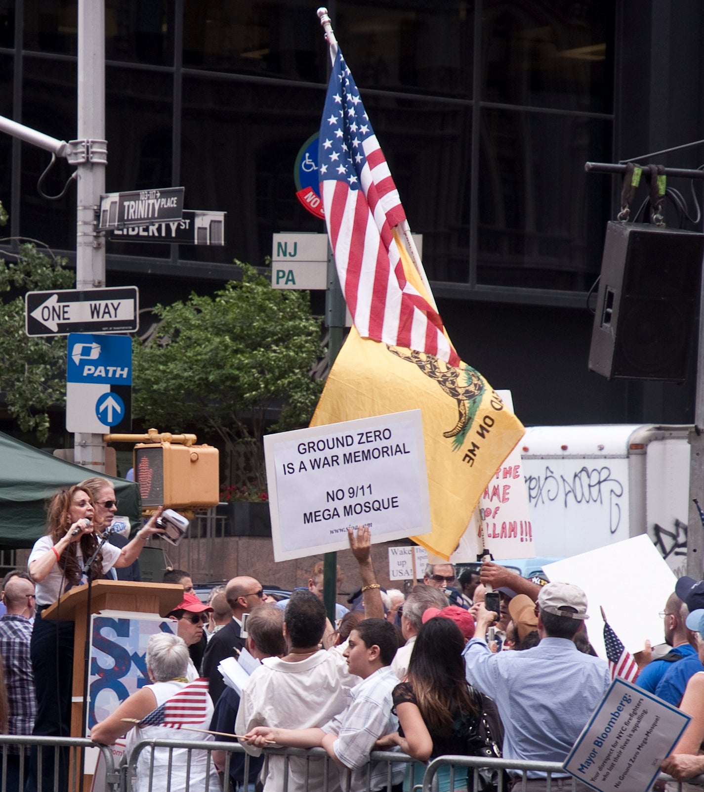 Pamela Geller speaks behind a podium at a rally. A protester's sign near the front of the crowd reads "Ground Zero is a War Memorial. No 9/11 mega mosque!"