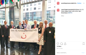 Screen shot of a post from the Instagram account of 'Save the Persecuted Christians,' in which members are standing with Ambassador-at-large for International Religious Freedom Sam Brownback, holding a white banner that black text that reads, "Save the Persecuted Christians" and a large font sized noon, an Arabic letter.
