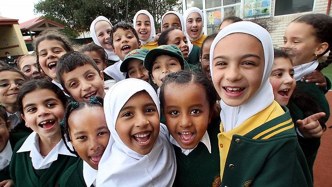 A group of children look at the camera and laugh. Some are wearing hijabs